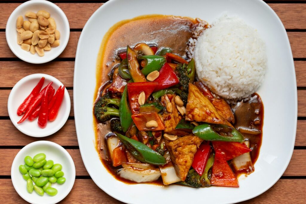 Thai Curry Rainbow dish with a serving of rice, assorted vegetables, and sprinkled peanuts on a white plate.