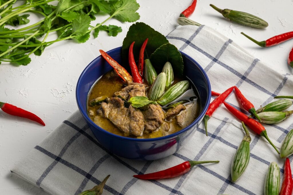 A bowl of Thai green curry featuring chicken and assorted vegetables on a white table.