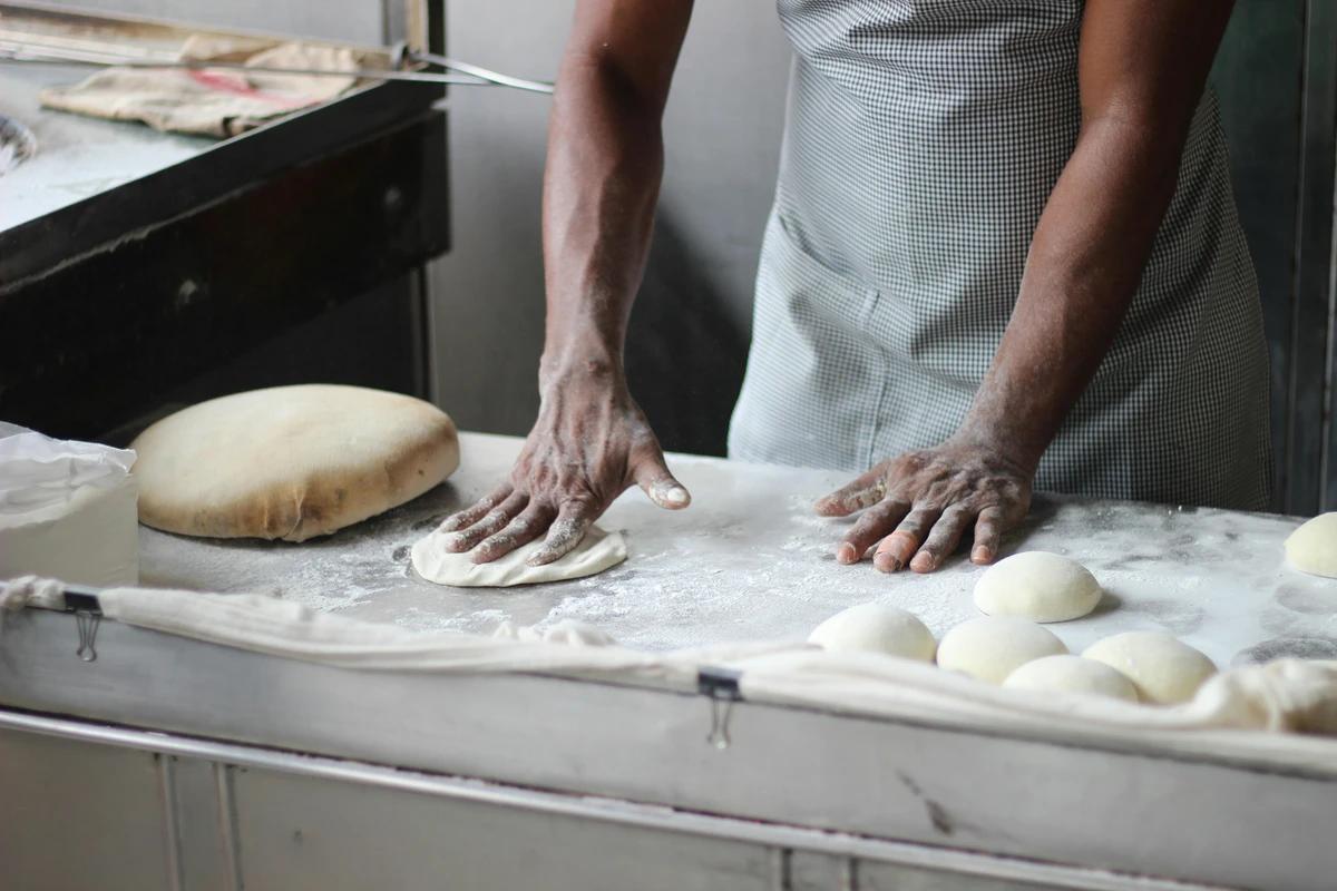 Baker kneading dough on a floured table during an artisan bread-making visit in a local bakery.
