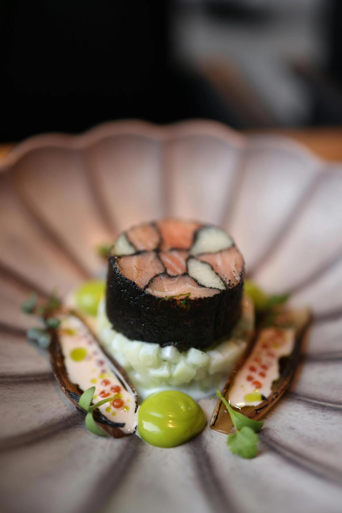 Elegant fine dining plate featuring a sushi-inspired salmon roll with gourmet sauce and garnish