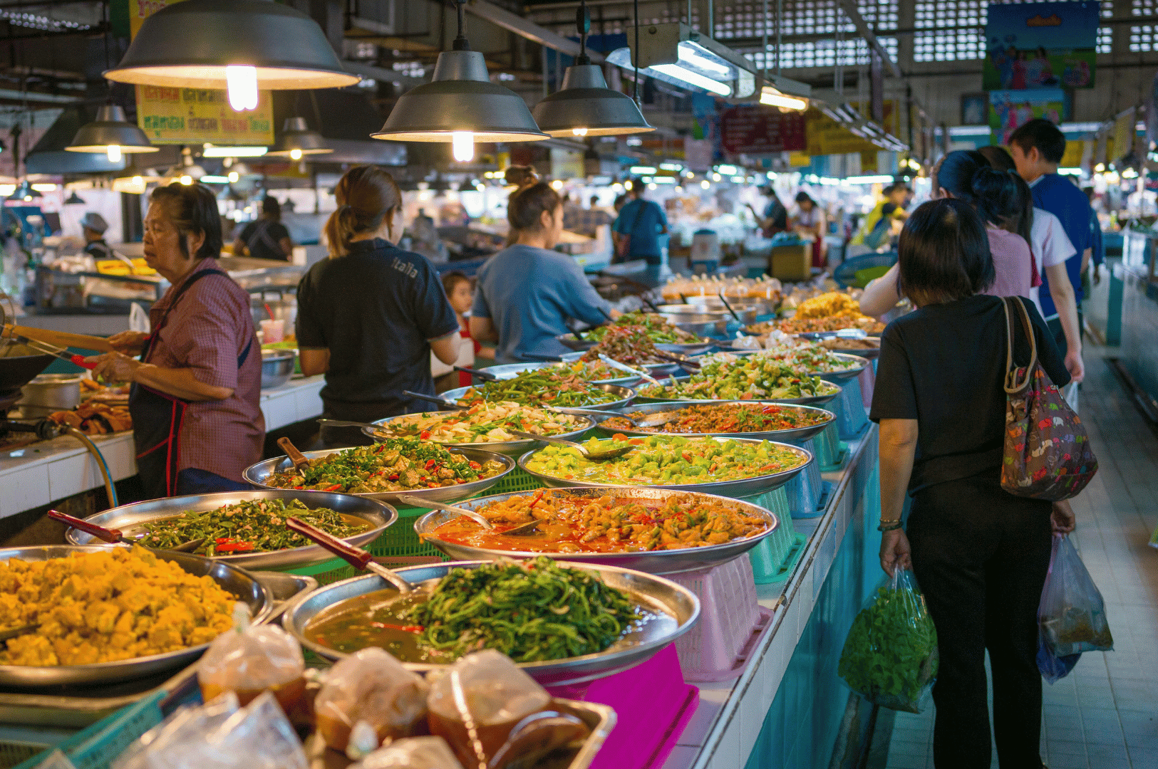 Vibrant Bangkok street food market bustling with locals and travelers browsing colorful trays of Thai curries, grilled meats, and stir-fried vegetables under warm hanging lights—capturing the sensory richness and communal energy of Thailand’s must-try culinary scene.