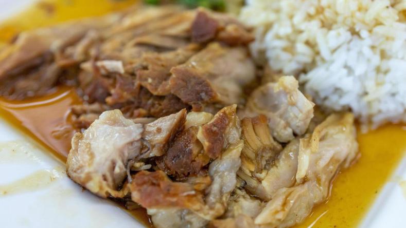 This is a close-up photograph of a savory meal, likely featuring tender, slow-cooked meat that is partially shredded and resting in a light, flavorful sauce.