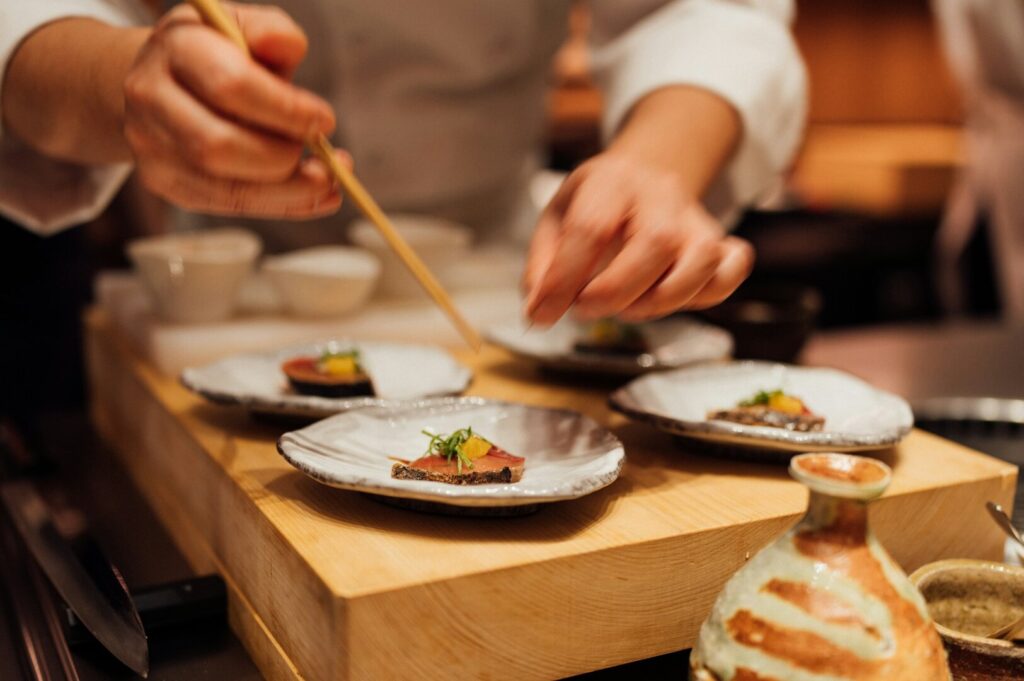 A chef skillfully prepares ingredients on a wooden cutting board in an intimate omakase setting in Singapore.