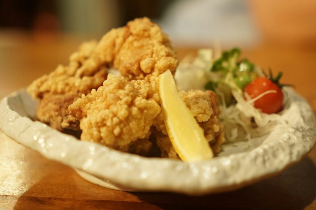 A serving of karaage fried chicken on a plate, garnished with a variety of fresh vegetables.