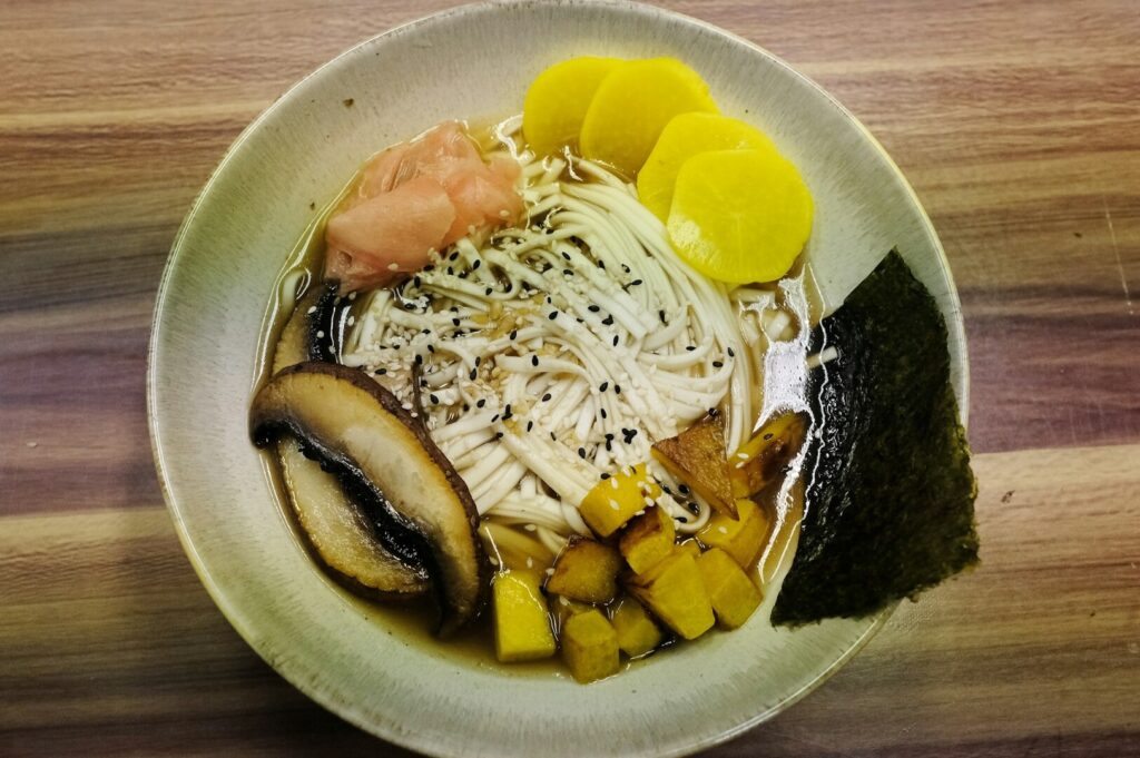 A vibrant bowl of noodles featuring assorted vegetables and mushrooms, highlighting a delicious plant-based umami taste.