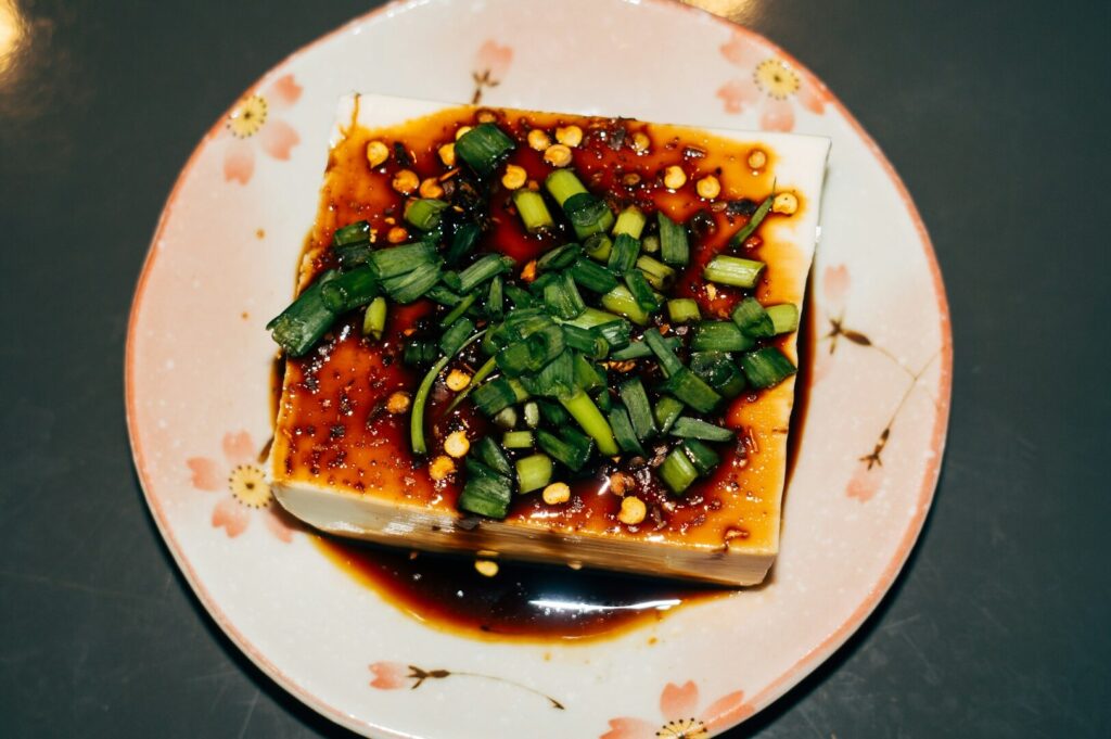 A serving of Mapo Tofu topped with fresh green onions on a white plate, representing Japanese cuisine.