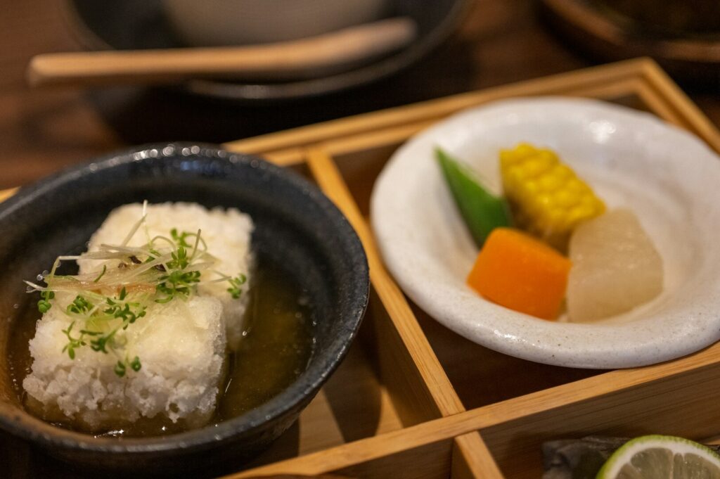 A wooden tray holds a bowl filled with rice and colorful vegetables, representing a delicious vegan umami meal.