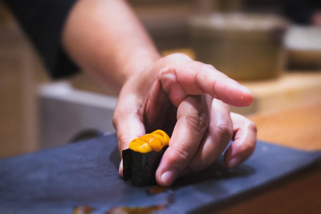 Japanese omakase sushi close-up featuring uni nigiri with seaweed wrap and rice, delicately presented by hand.