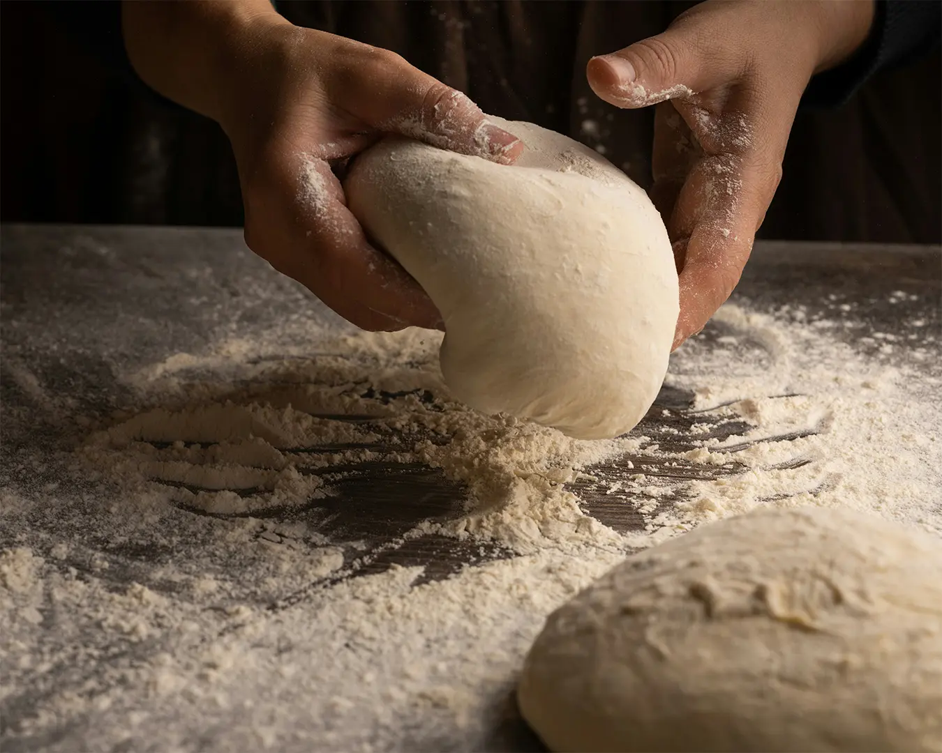 Close-up of a baker’s hand holding freshly kneaded dough lightly coated with flour, highlighting the soft texture and the preparation process before baking.