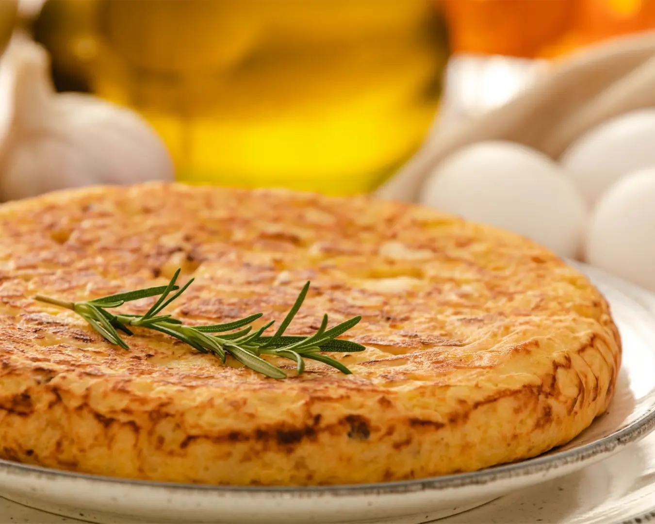 A golden Spanish tortilla served on a plate, showcasing thick layers of tender potatoes bound in soft egg, lightly crisped on the outside and rustic in presentation.