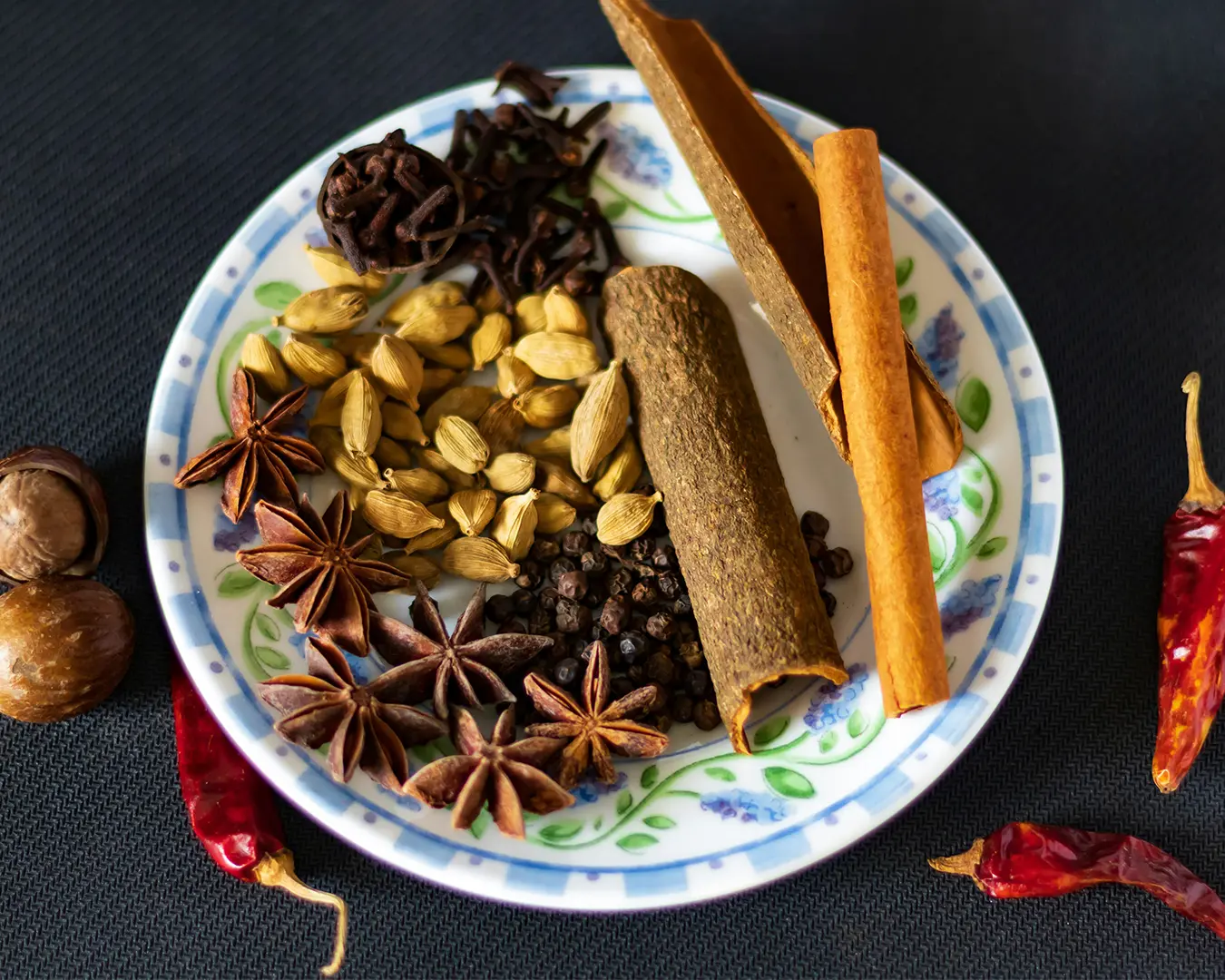 An assortment of aromatic spices arranged on a plate, including cinnamon sticks and other fragrant seasonings, showcasing the essential ingredients that contribute to the depth and warmth of curry flavour.