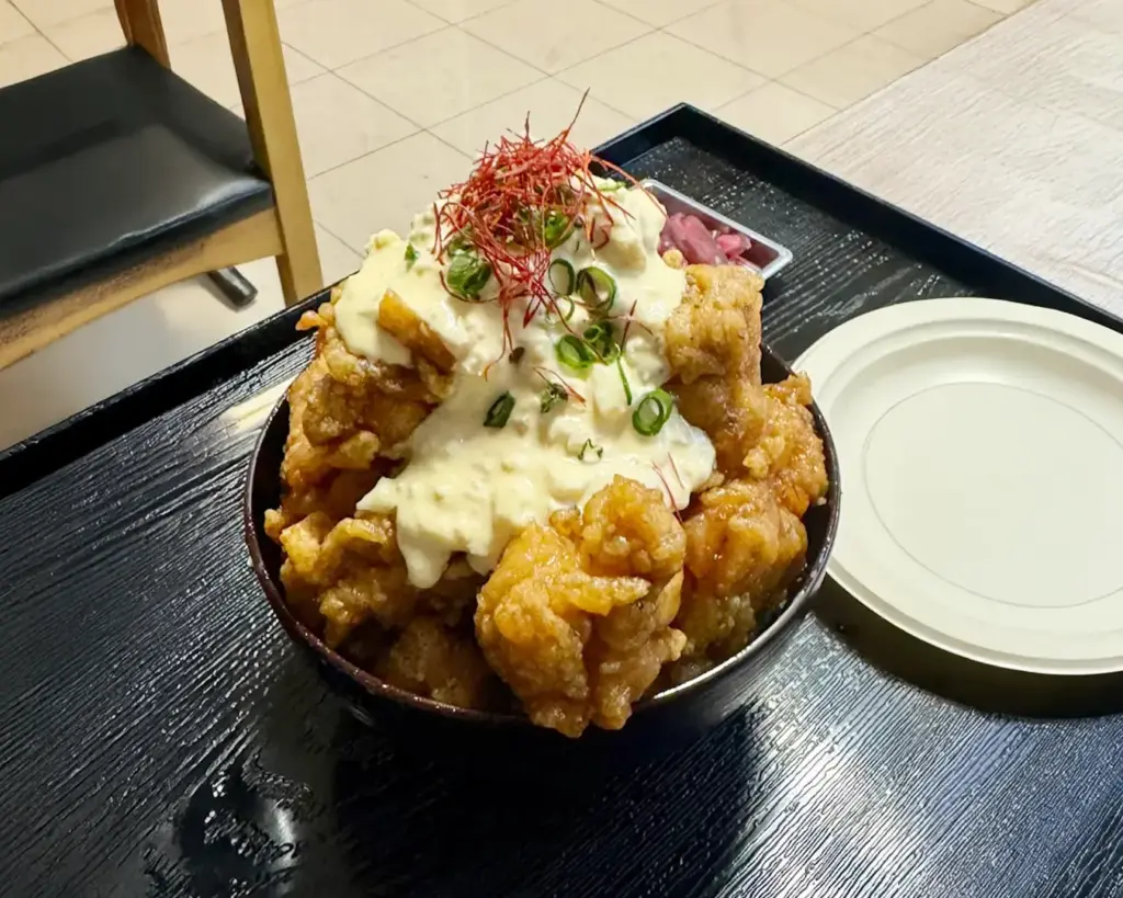 A bowl of chicken nanban don featuring crispy fried chicken coated in a sweet and tangy sauce, served over warm rice and topped with creamy tartar sauce and shredded cabbage.