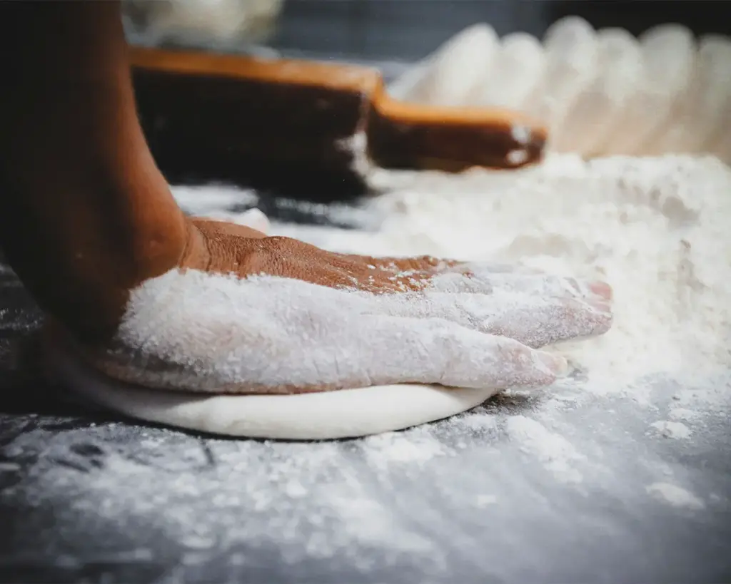 Close-up of hands pressing and shaping soft dough on a floured surface, showing the traditional technique used to prepare bread before baking.