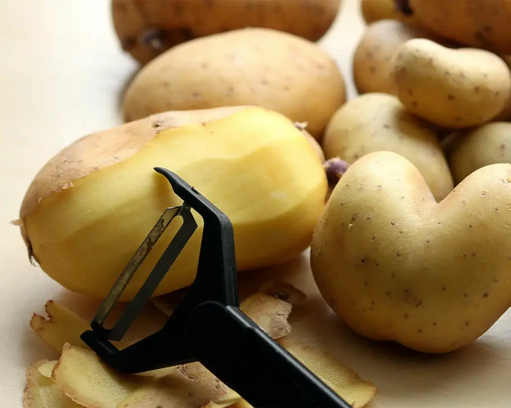 Close-up of a hand carefully peeling a fresh potato, revealing the smooth pale surface beneath the skin as part of the preparation process for cooking.