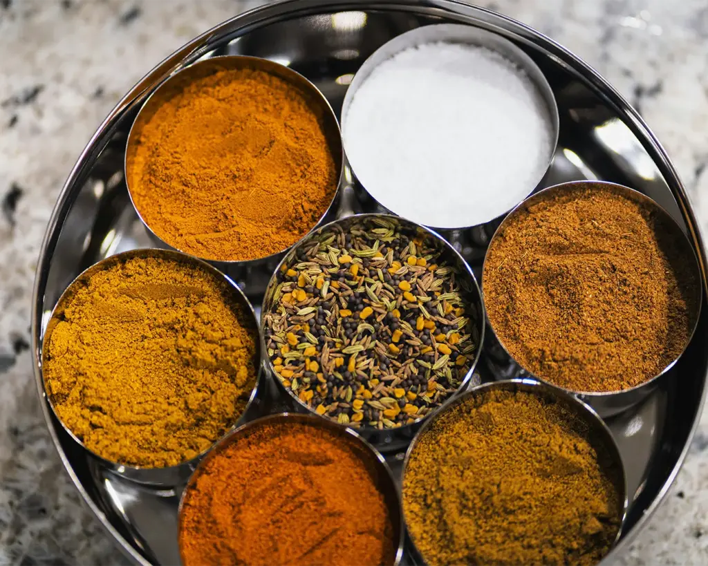 Several varieties of curry powder displayed side by side, each with different shades of golden yellow and deep brown, highlighting the diverse spice blends used in different curry preparations.