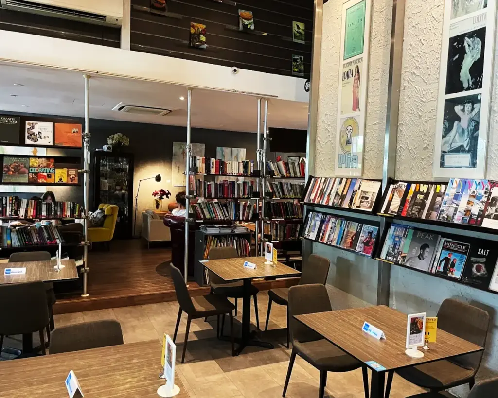 A thoughtfully arranged café designed for co-working, featuring shelves of books, spacious tables, and a peaceful environment ideal for focus and productivity.