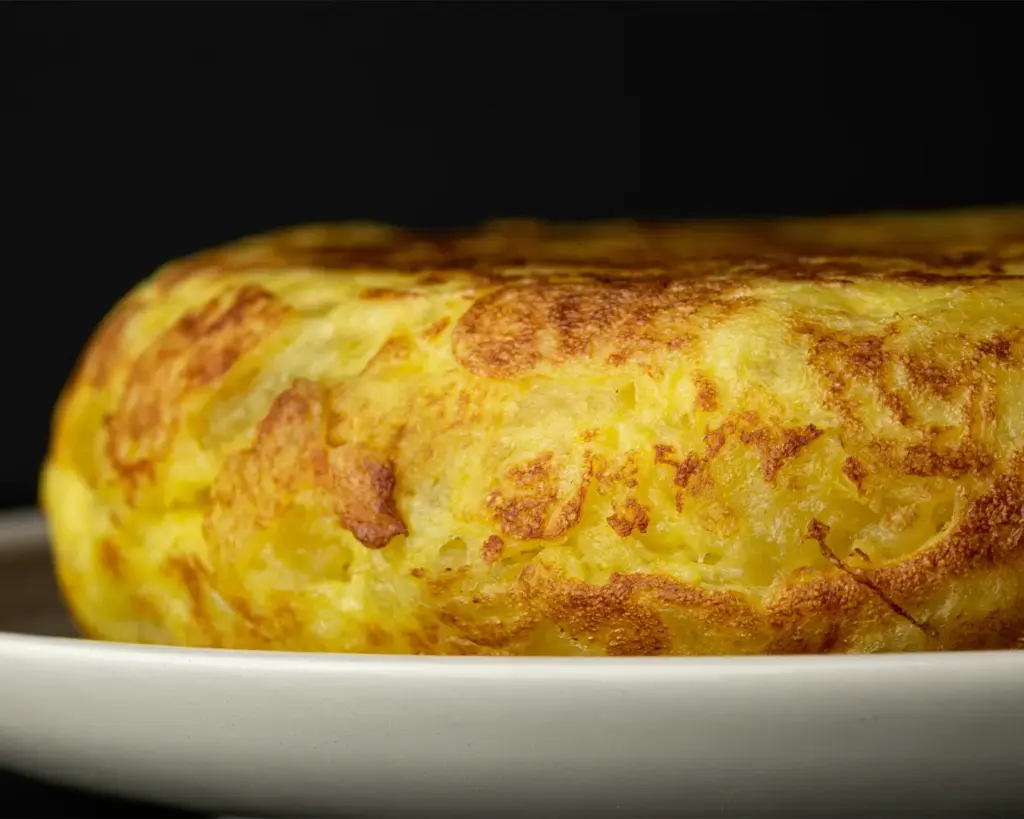 A beautifully cooked Spanish omelette plated and ready to serve, with a soft centre and golden exterior highlighting the classic combination of eggs, potatoes, and onions.