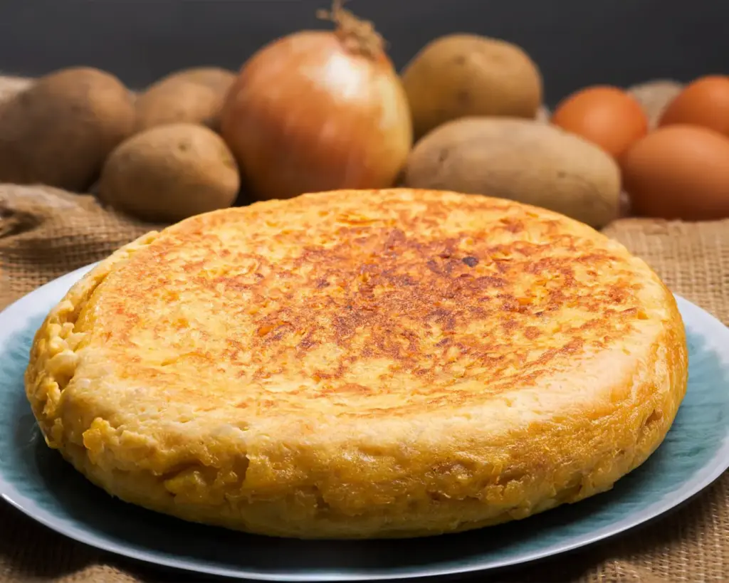Traditional Tortilla de Patatas presented on a plate, thick and rustic, with visible layers of potatoes set in eggs and a lightly caramelised surface.