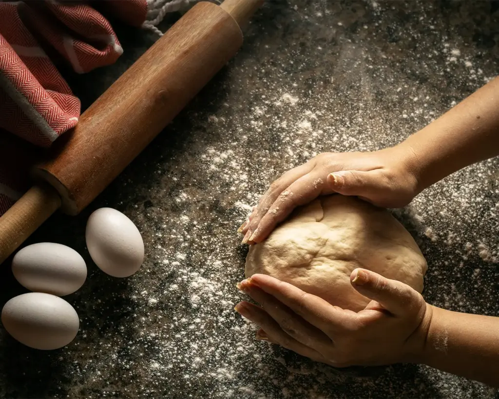 Hands kneading dough on a lightly floured work surface, illustrating the artisanal process of mixing and shaping dough before it becomes bread.