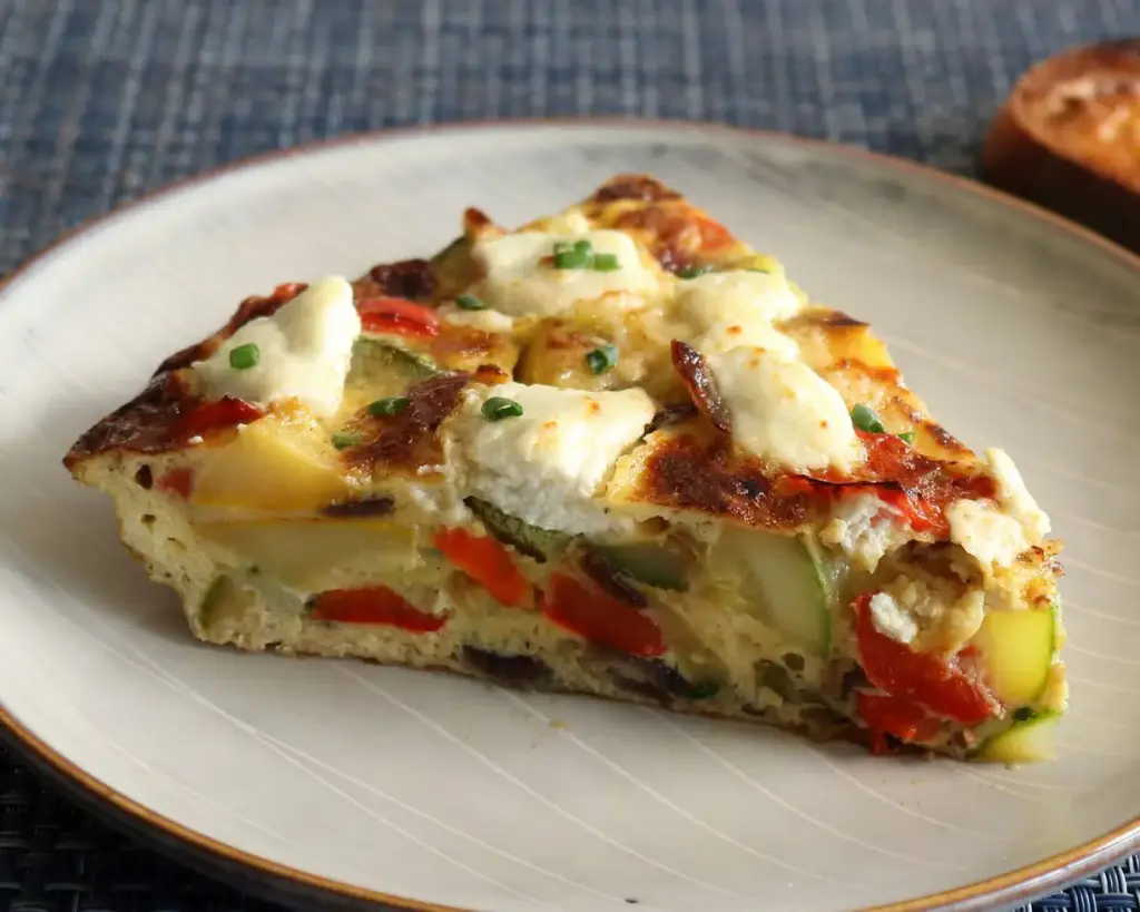 A plate of sliced Italian frittata, showcasing golden wedges of baked eggs mixed with vegetables and herbs. The frittata is lightly browned on the surface, revealing a soft and fluffy interior.