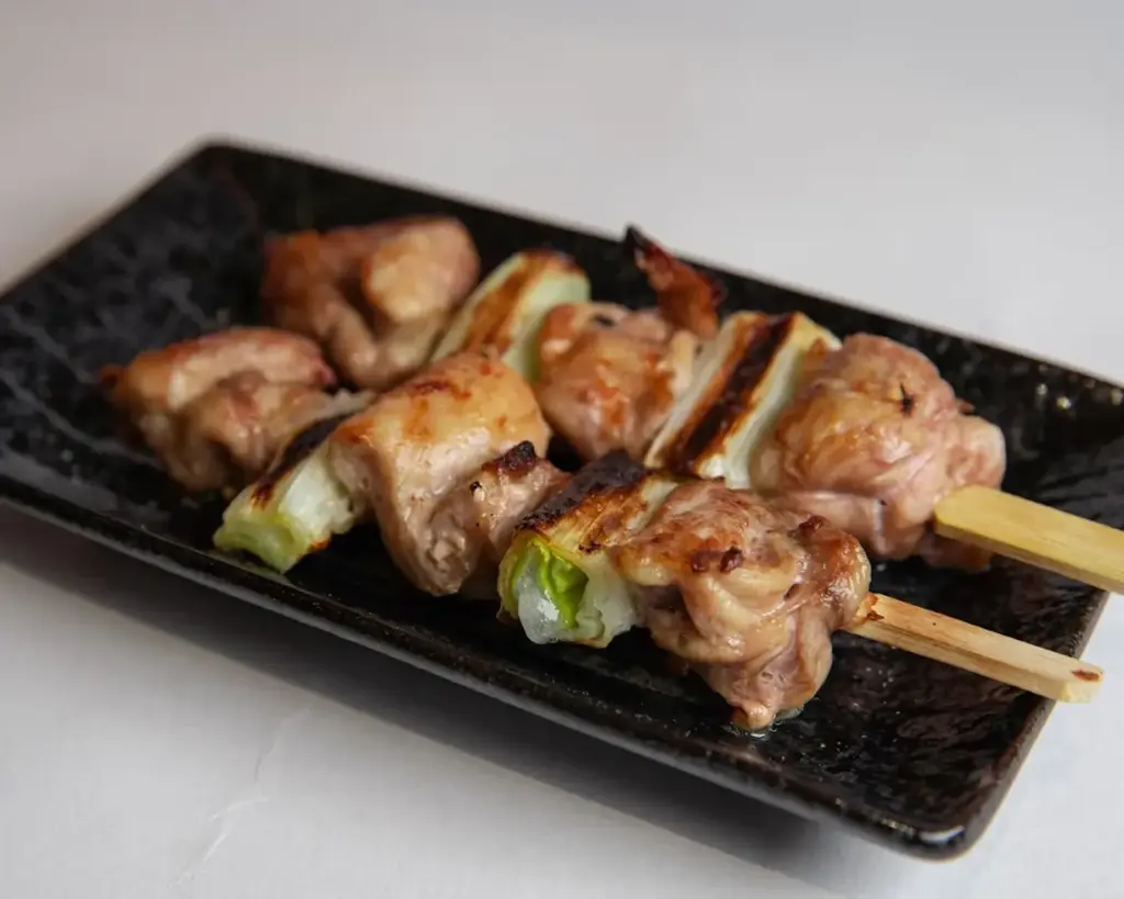 Grilled chicken skewers glazed with savoury sauce and lightly charred edges, served hot on a plate. The skewers showcase tender, juicy pieces of chicken grilled over high heat, giving them a smoky aroma and caramelised finish.
