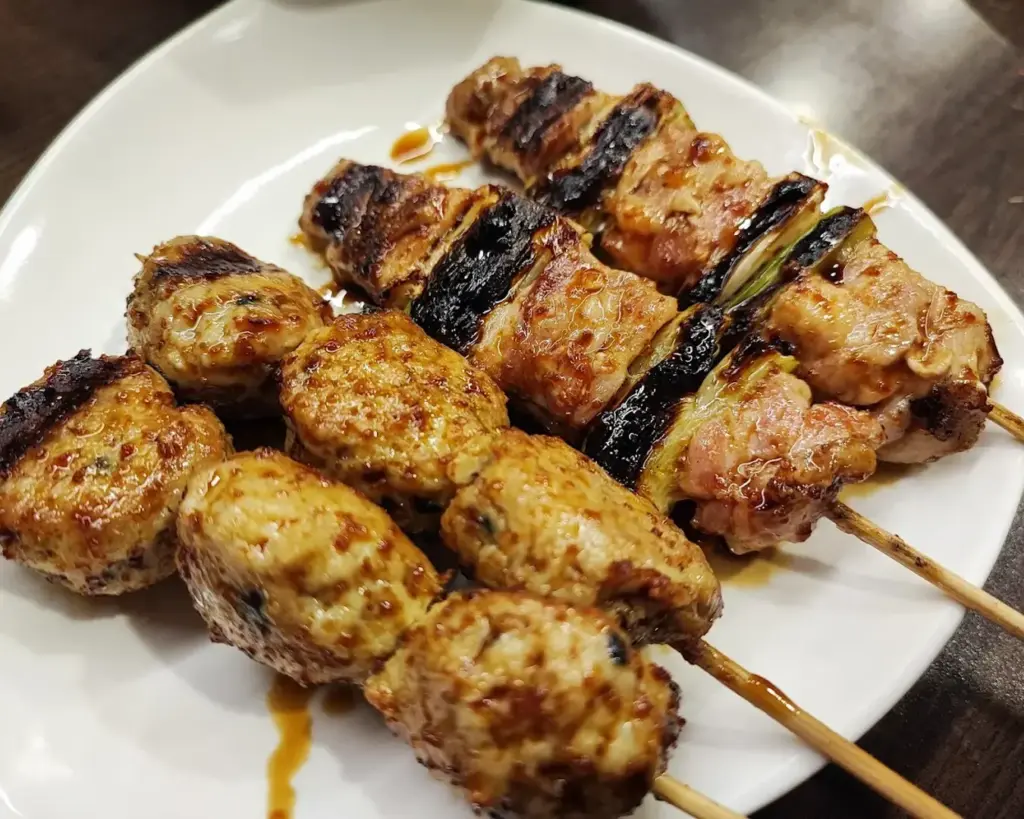 Grilled skewers of seasoned meat on a white plate, glistening with sauce and char marks, evoke a savory and appetizing dining experience.